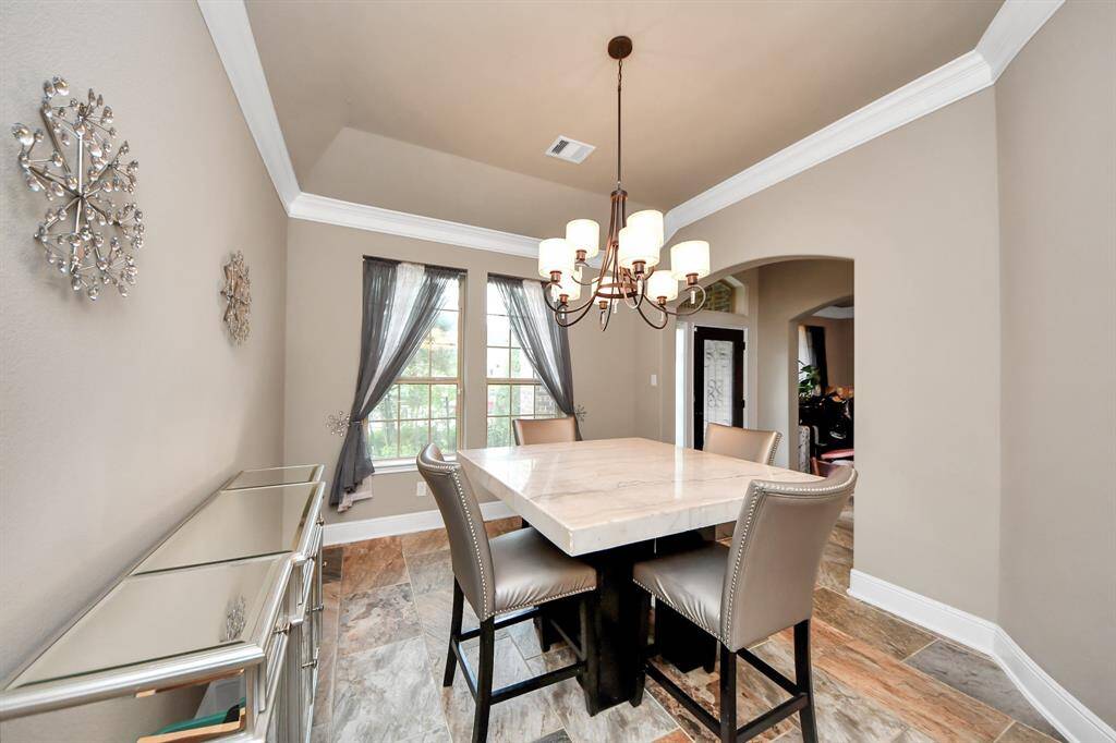This dining room has neutral walls, decorative accents, and large windows that offer ample natural light. The arched doorway leads to another room, enhancing the open feel.