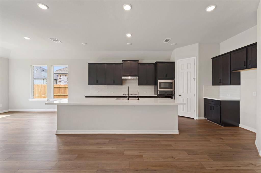 This light and bright kitchen features a large quartz island, white cabinets, a large sink overlooking your family room, recessed lighting, and beautiful backsplash.
