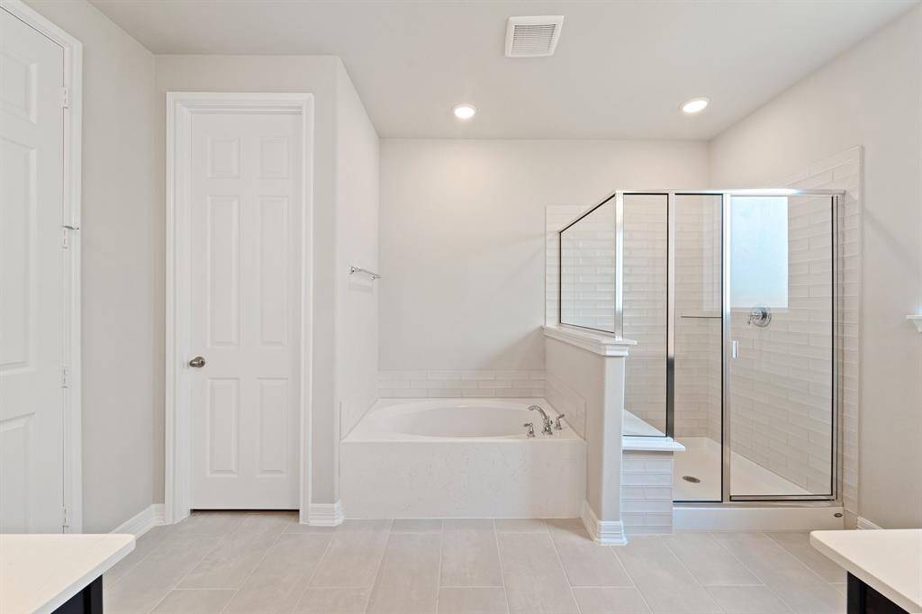 This additional view of your primary bathroom features tile flooring, fresh paint, walk-in shower, a separate garden tub, and a large walk-in closet.