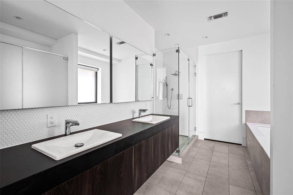 The modern primary bathroom features double sinks, large mirrors, and a spacious glass-enclosed stand-in shower.