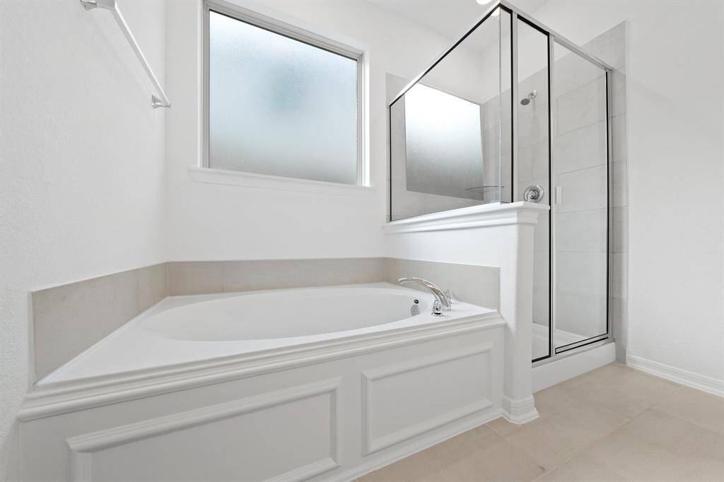 This additional view of your primary bathroom features tile flooring, fresh paint, walk-in shower, a separate garden tub, and a large walk-in closet.