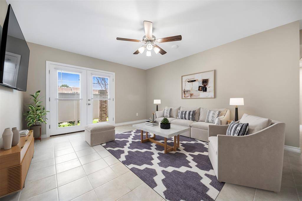 The bright and inviting living room featuring a neutral color palette, ceiling fan for comfort, and double doors that open to the patio—blending indoor comfort with outdoor charm.(This photo is virtually staged)