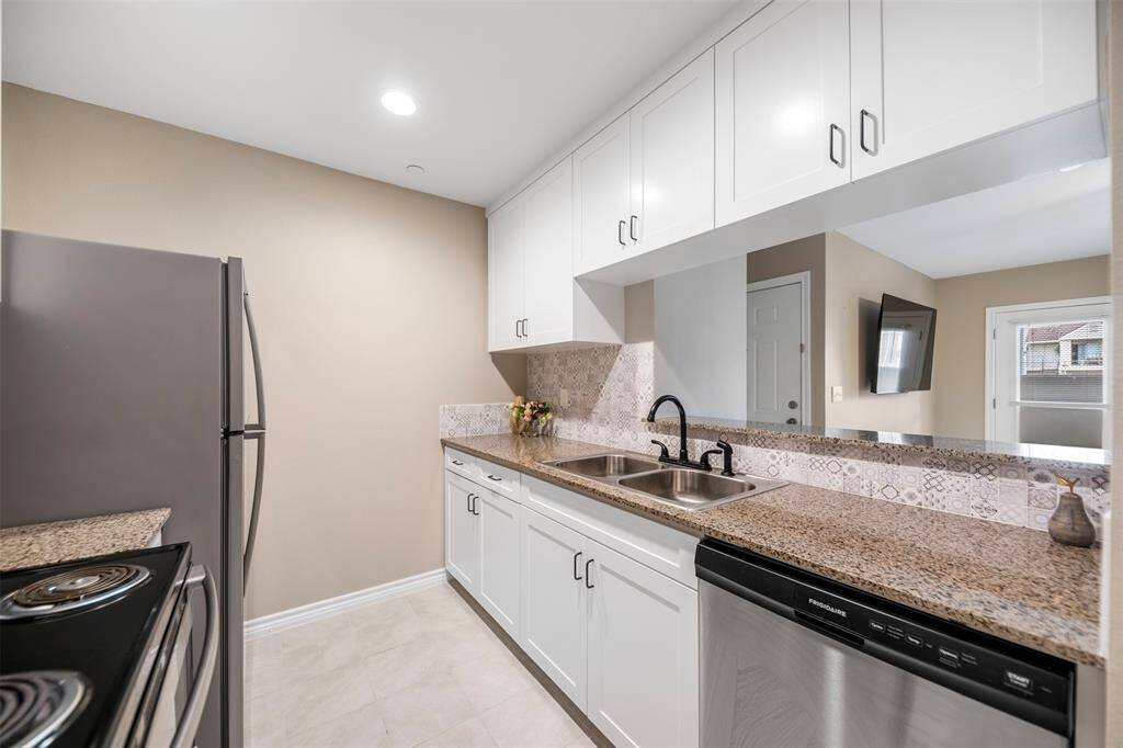 Another view of the stylish kitchen showcasing the built-in stainless steel dishwasher, white cabinetry with striking black hardware, and a clean, cohesive design that’s both practical and elegant.