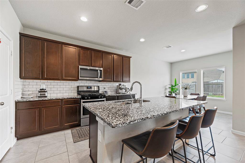 Now into the kitchen. Features include granite countertops paired with a coordinating tile backsplash, stainless steel appliances, rich cabinets, under cabinet lighting, recessed lighting, and a sprawling island with breakfast bar seating.