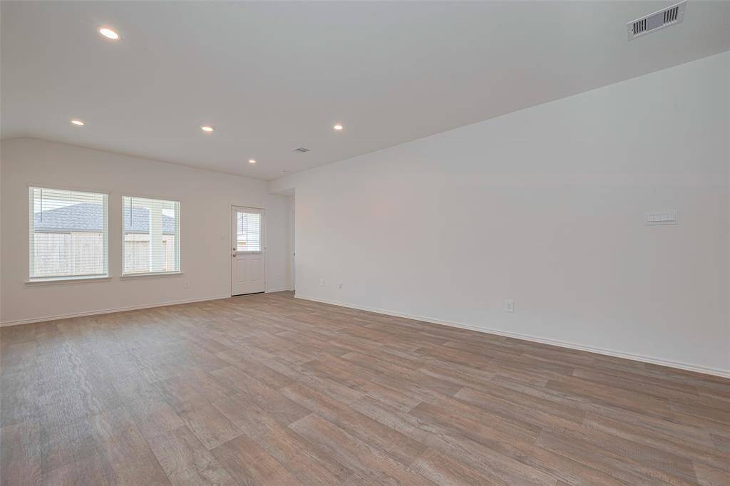 The spacious living room is filled with light from large windows and a glass paneled door that opens to the backyard. Recessed lighting highlights the rich wood-look flooring, creating an inviting space for relaxation and entertaining.