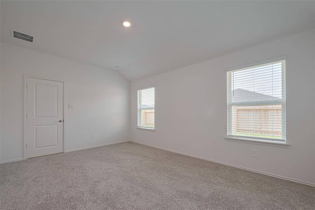 The primary suite is a spacious haven with a gently sloping ceiling, plush carpeting, and large windows that frame backyard views and invite serene daylight.