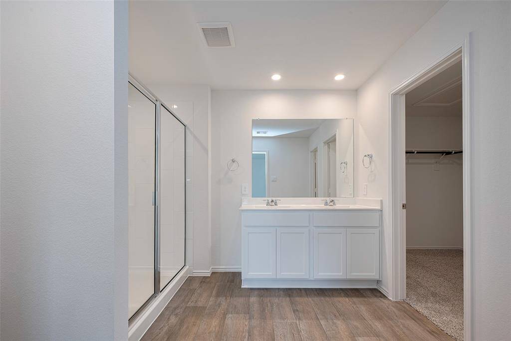 The primary bathroom features a dual-sink vanity with white cabinetry, a broad mirror, and an enclosed shower with nearby open shelving. A connecting full entry closet adds everyday convenience.