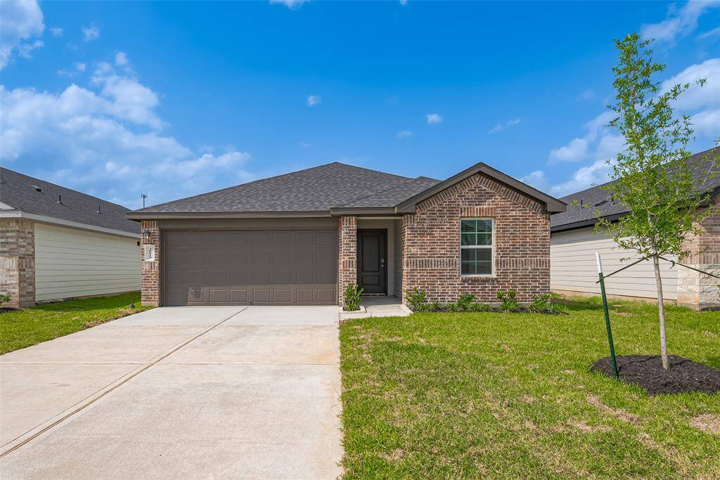 A smooth, wide driveway leads to the two-car garage, where the rich-toned garage door complements the front entryway tucked into the facade. A young tree and neatly manicured lawn add fresh curb appeal to the timeless brick exterior.