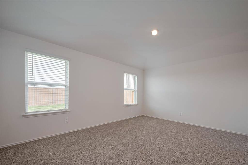 This spacious primary bedroom features a soft sloped ceiling and expansive windows that invite in the daylight. The carpeting and airy dimensions create a serene personal space.