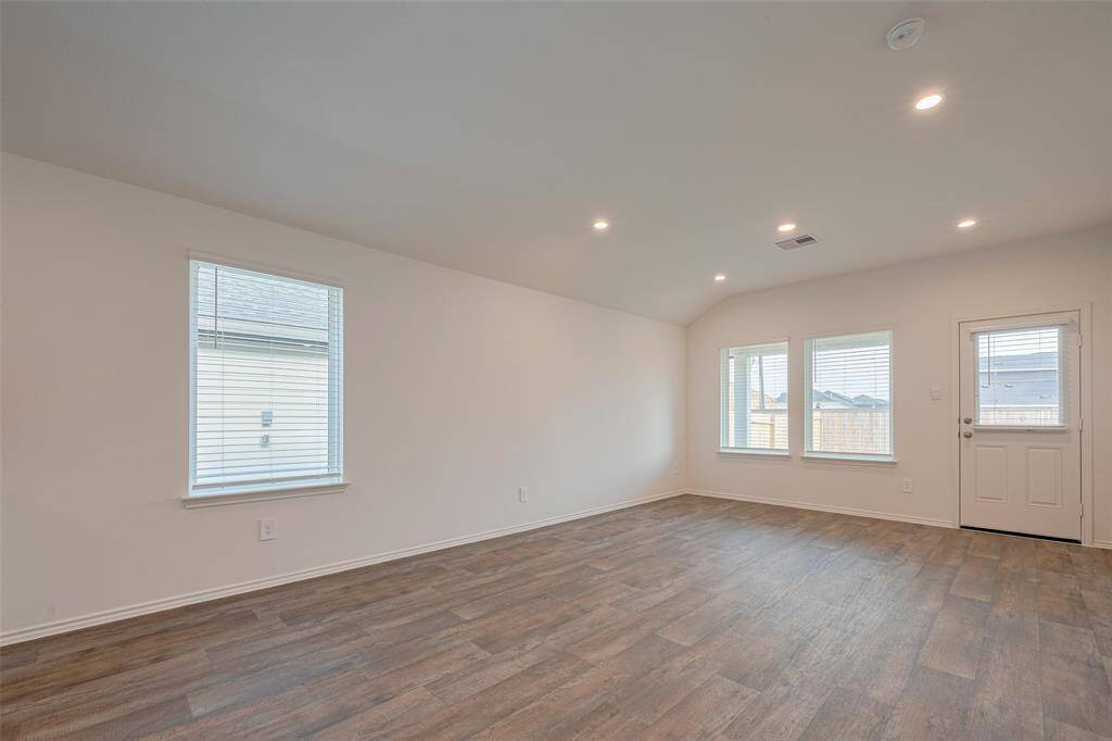 A bright and airy living room features large windows and a glass-paneled back door that usher in natural light. Soft lighting and rich-toned luxury vinyl plank flooring create a cozy yet contemporary setting.