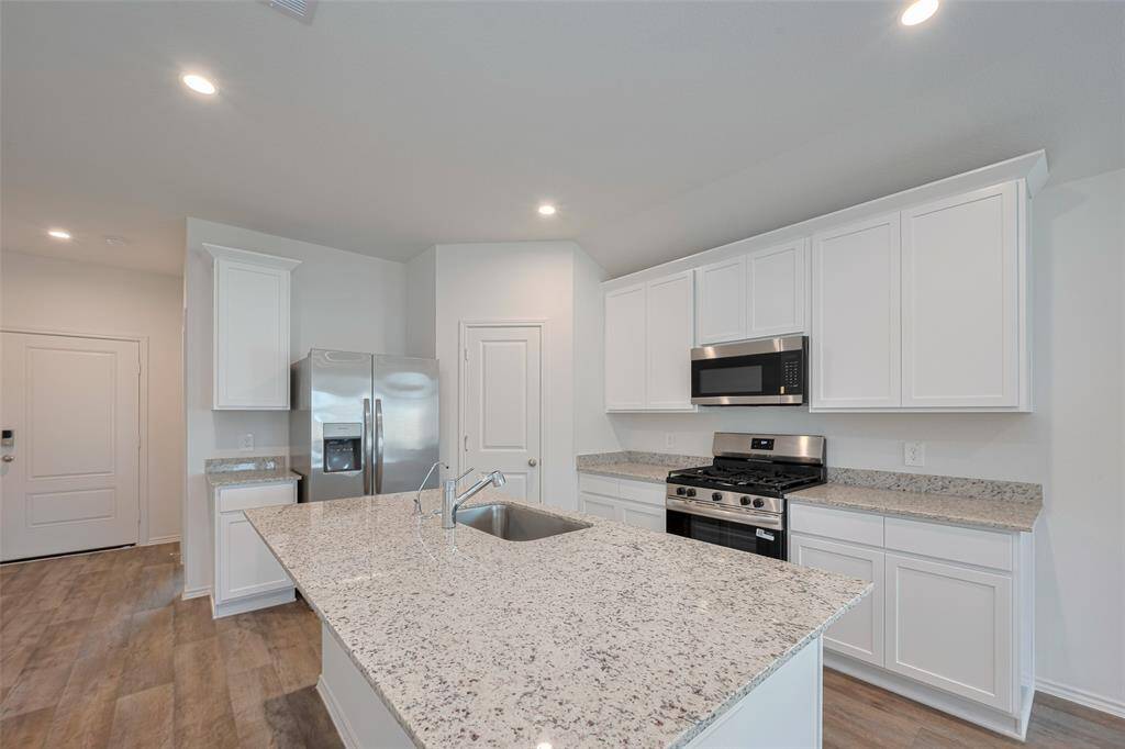Crisp white cabinetry—both overhead and below—provides abundant storage, while granite countertops offer ample room for cooking, entertaining, or display.