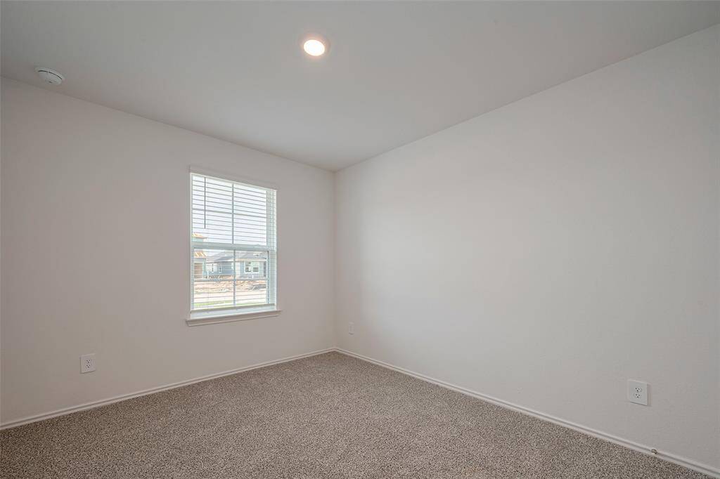This spacious bedroom is carpeted and filled with daylight from a large window, creating a comfortable retreat.