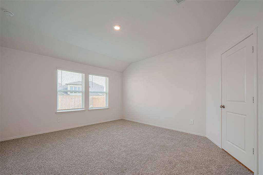 A generously sized primary suite features soft carpeting, a gentle ceiling slope for added dimension, and expansive windows that bring in plenty of natural light.