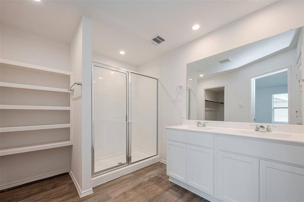 The ensuite bathroom boasts a dual-sink vanity with white cabinetry and a wide mirror above. A separate glass-enclosed shower sits beside open shelving.