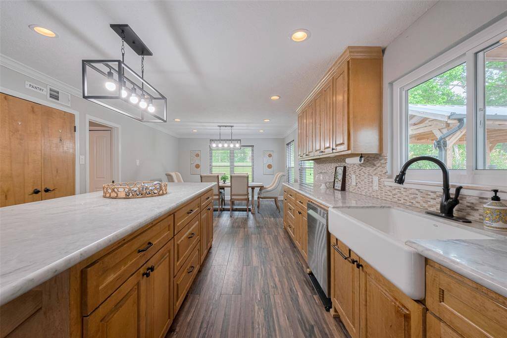 The kitchen combines style and functionality, featuring a large marble island, perfect for prepping meals or casual dining. The open layout flows seamlessly into the dining area, with beautiful cabinetry, a farm sink, and modern fixtures. A window above the sink lets you gaze out at the covered patio and pool area, creating a bright and cheerful space for cooking and entertaining.