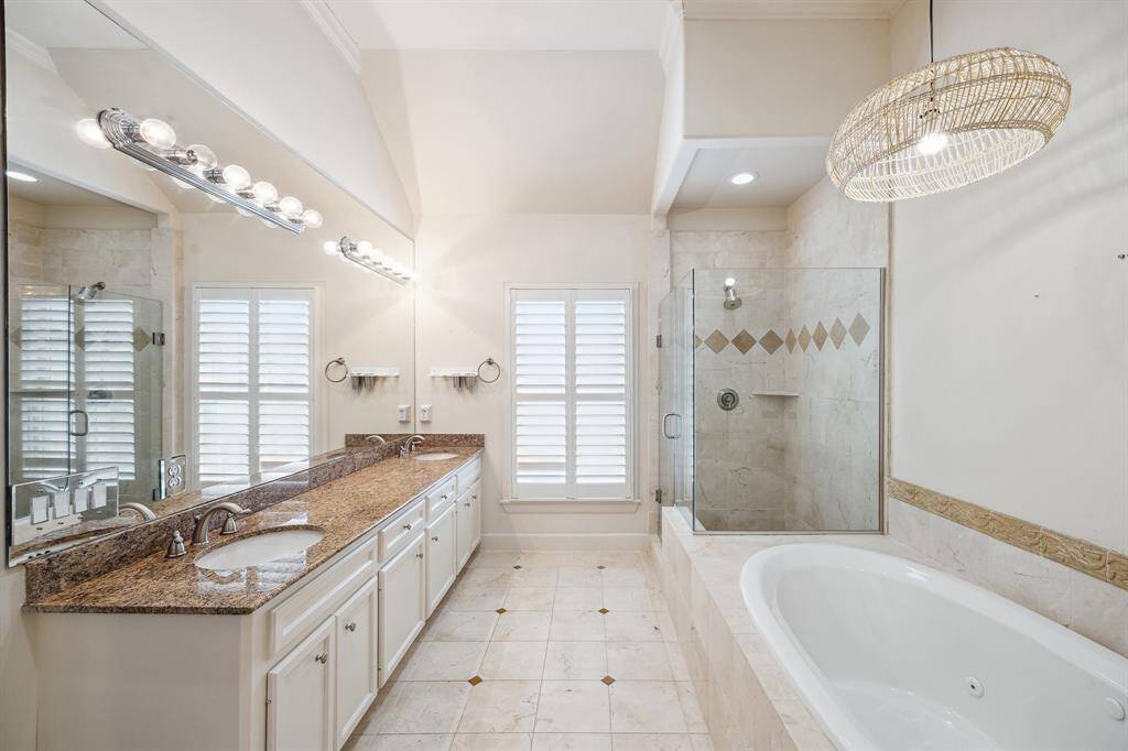 This expansive bathroom features a long mirror with inset lighting, extensive custom site built storage vanity and a lengthy granite countertop, and dual undermount sinks. The large shower includes a built-in bench, a storage shelf, recessed lighting, and a seamless glass enclosure. Note: the vaulted ceiling and crown molding, a consistent design element throughout all rooms and bathrooms in the home.