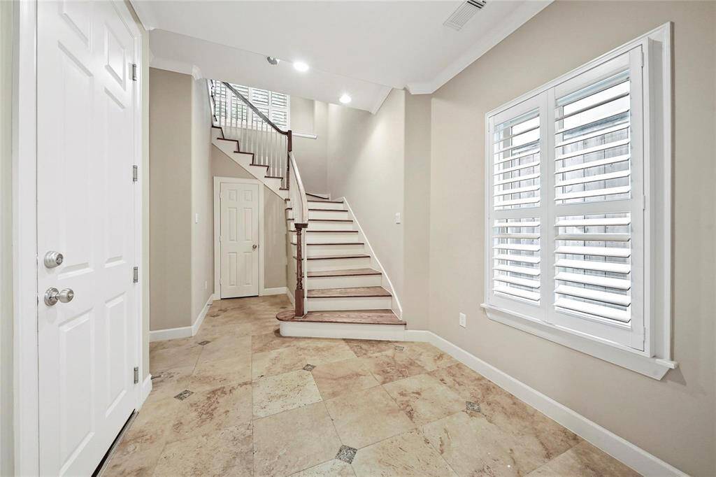 Step into a bright and airy foyer that welcomes guests with its spacious design. The wide staircase, featuring beautiful hardwoods invites you to the main level. The door to the garage is on the left, while the recessed doorway leads to a first-floor bedroom and full bath. The door in the center of the photo now reveals a wine closet.