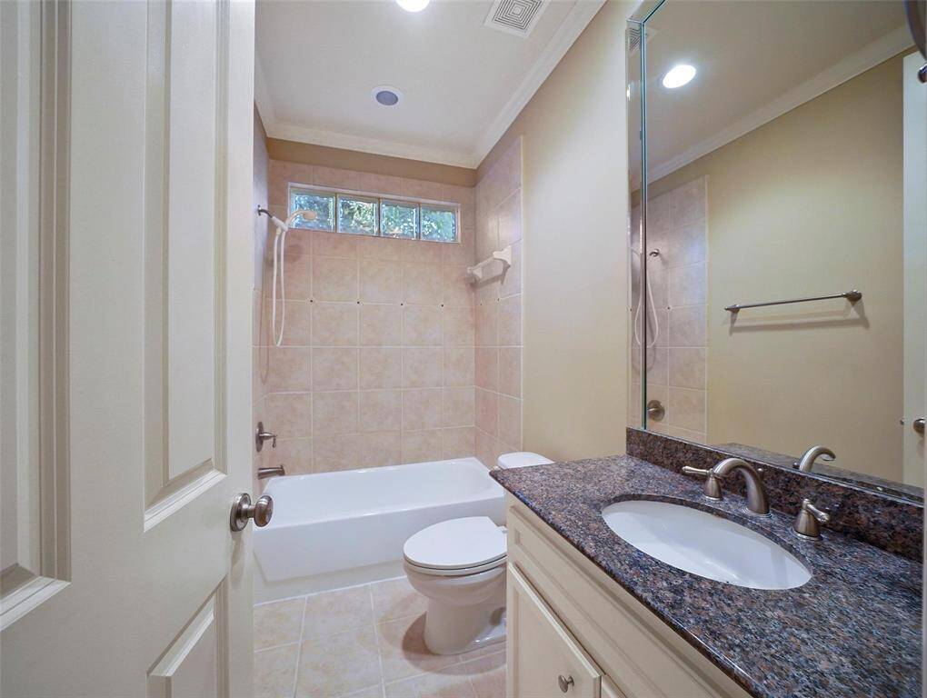 This 1st floor en-suite full bathroom features a custom site-built vanity, a granite countertop, an undermount sink, crown molding, and a tub/shower combo with a glass block clerestory window that allows natural light to filter in.