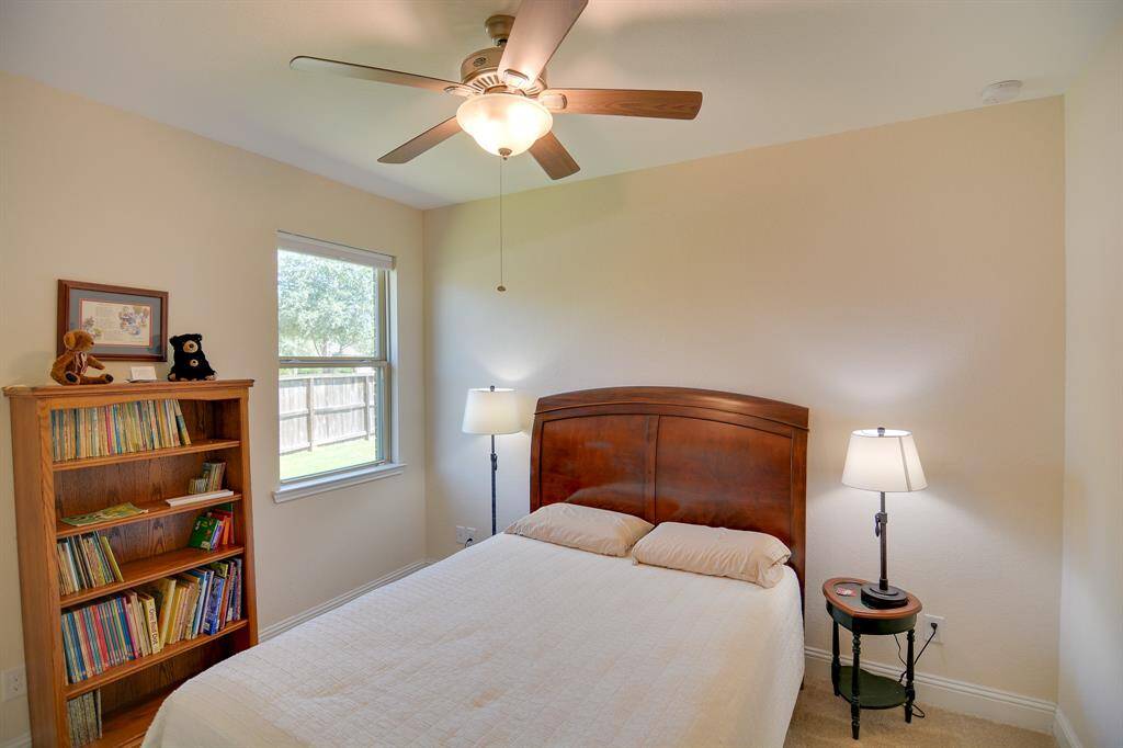 Secondary bedroom features plush carpet, neutral paint, dark stained ceiling fan with lighting and large window with natural light.