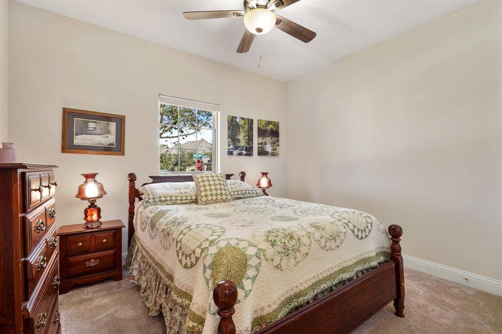 Secondary bedroom features plush carpet, neutral paint, dark stained ceiling fan with lighting, large window with natural light and plenty of space to design to your liking.