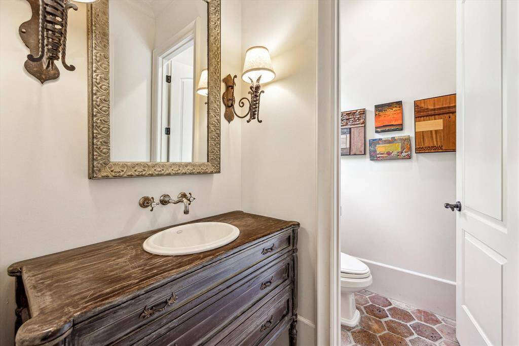 Step into one of two half baths - this one is conveniently located just off the entryway in the front of the house. This exquisite space features a rich wooden vanity and brick floors.