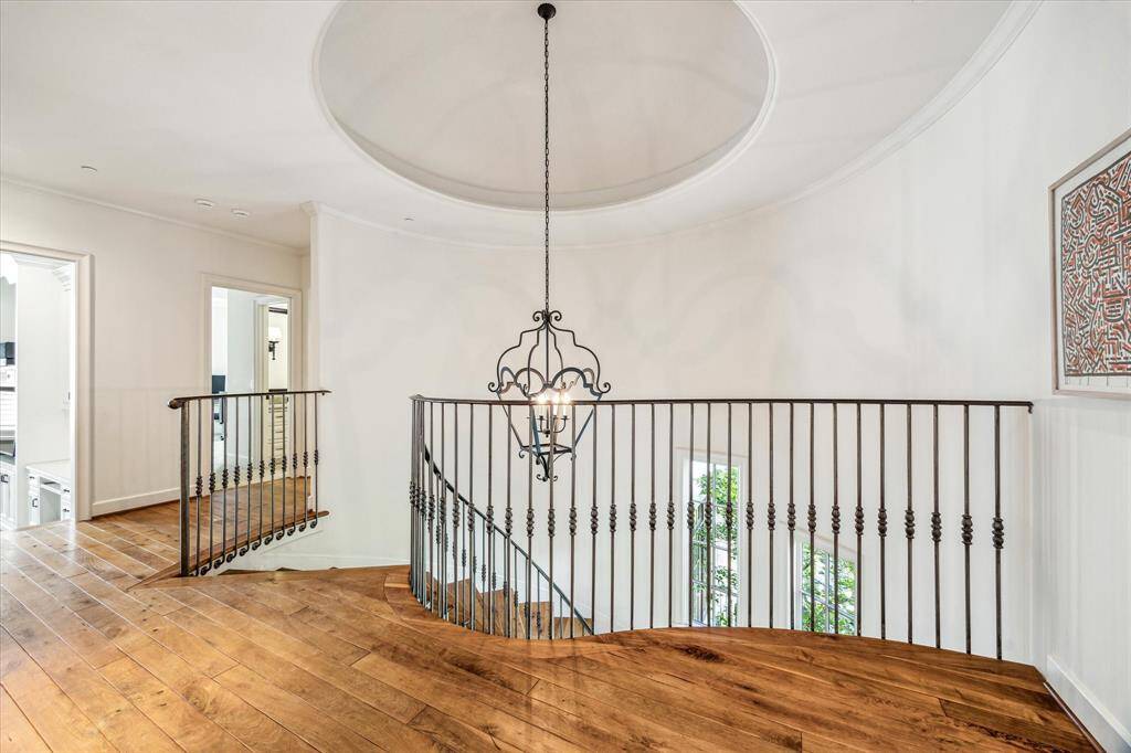 Spacious landing at the top of the elegant staircase, featuring a graceful wrought iron railing, stunning chandelier, warm wood floors, and a domed ceiling.