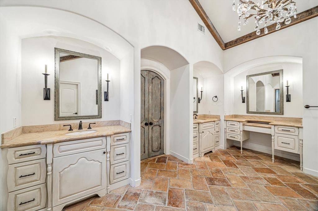 His/her vanities, offering ample space and elegance for daily routines. The reclaimed wood beams on the ceiling add a touch of rustic charm, perfectly complementing the gorgeous brick-style flooring that enhances the rooms sophisticated ambiance.