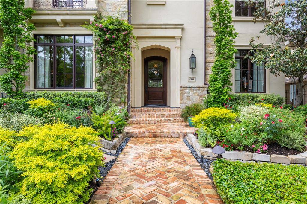 Stunning curb appeal at 4904 Laurel St., featuring vibrant shrubs, climbing vines, and a charming brick-paver walkway leading to a grand stone entryway with timeless architectural details.