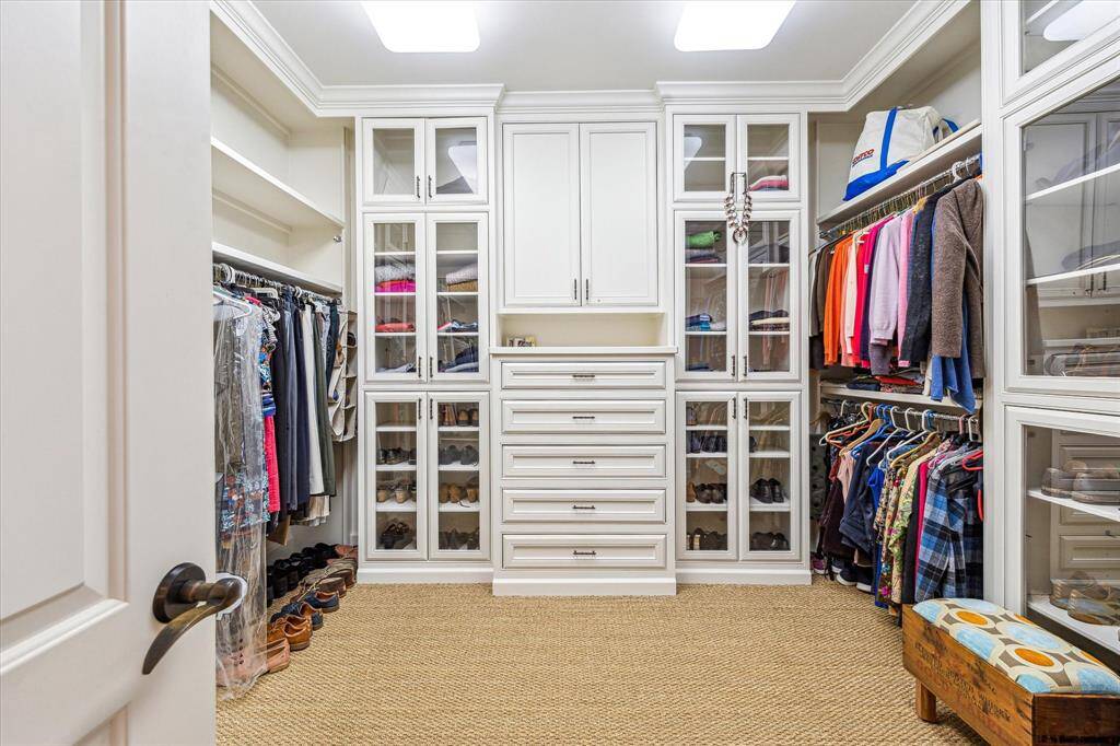 Expansive primary closet, one of the his-and-hers pair, offers a luxurious and organized retreat with elegant glass-fronted built-ins, ample drawers, and cabinets for seamless storage.