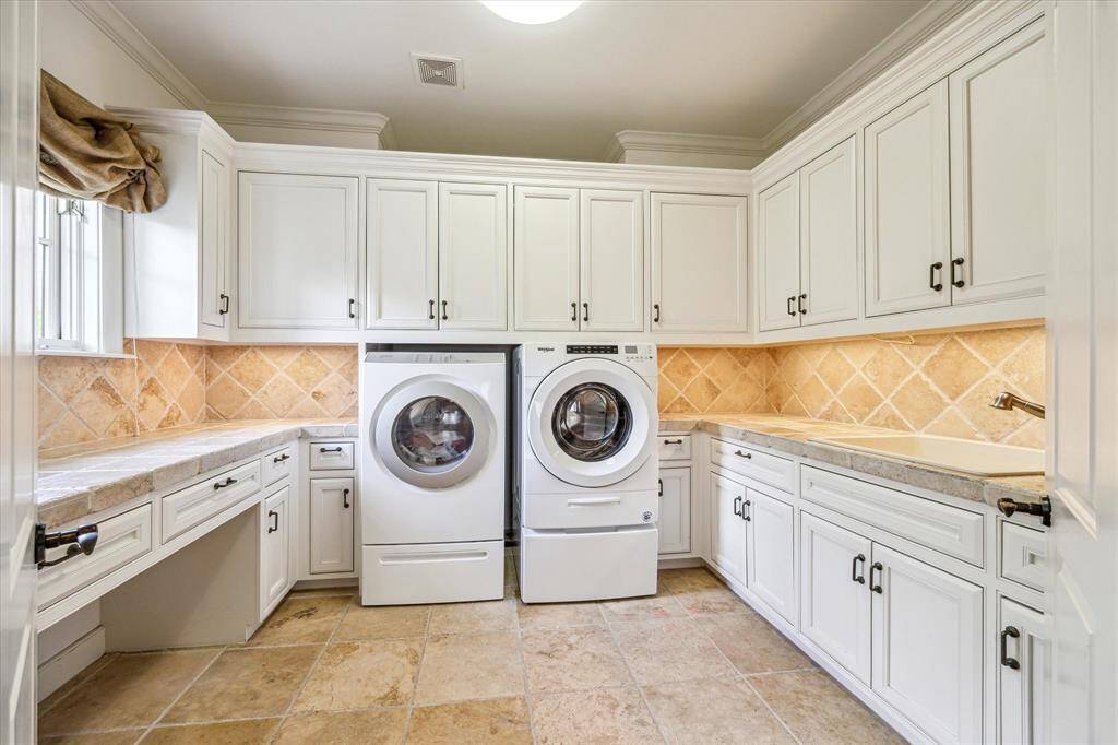 Spacious laundry room combines beauty and functionality, featuring a sink, convenient desk/craft area for added versatility. Elegant cabinetry provides ample storage, while a window allows natural light to brighten the space. The double-door entry enhances accessibility, making this well-designed room a practical and stylish.