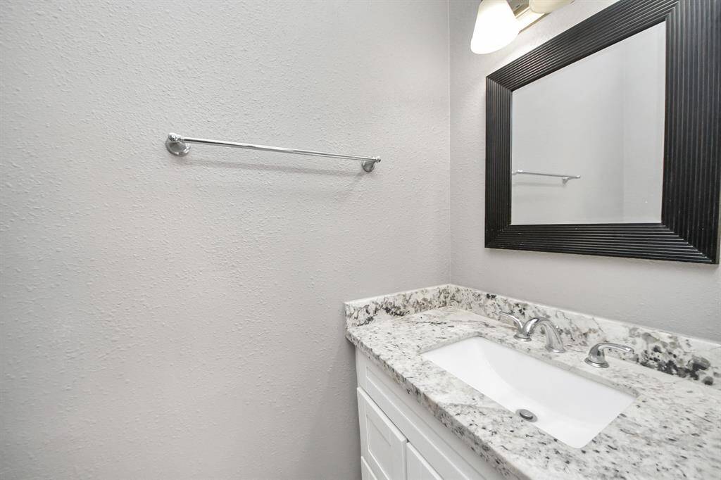 This bathroom features a sleek design with a granite countertop, undermount sink, modern fixtures, and a large framed mirror. The neutral walls add a bright and clean feel.