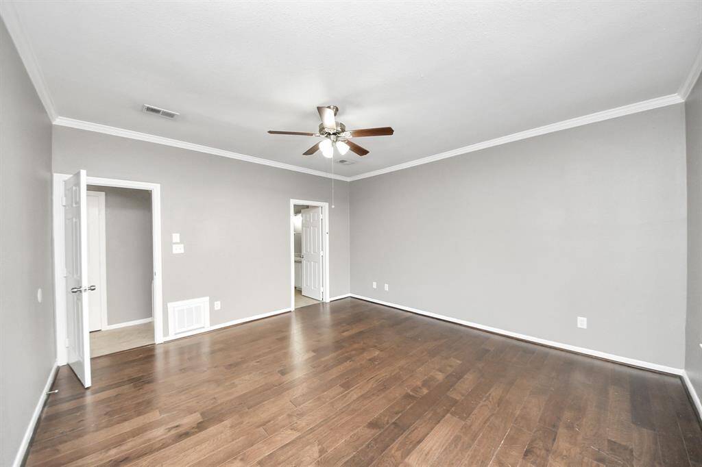 This room features hardwood floors and neutral gray walls with white trim. It includes a ceiling fan and multiple doorways, offering a bright and versatile space suitable for various uses.