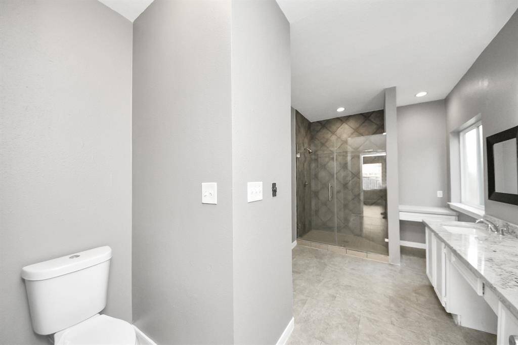 Spacious modern bathroom featuring a glass-enclosed shower, sleek gray walls, and a long marble countertop with dual sinks.