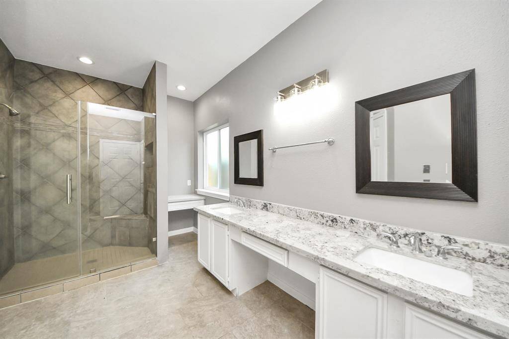 This bathroom features a spacious walk-in shower with floor-to-ceiling tiles, a large dual-sink vanity with marble countertops, modern lighting, and a neutral color palette for a contemporary feel.