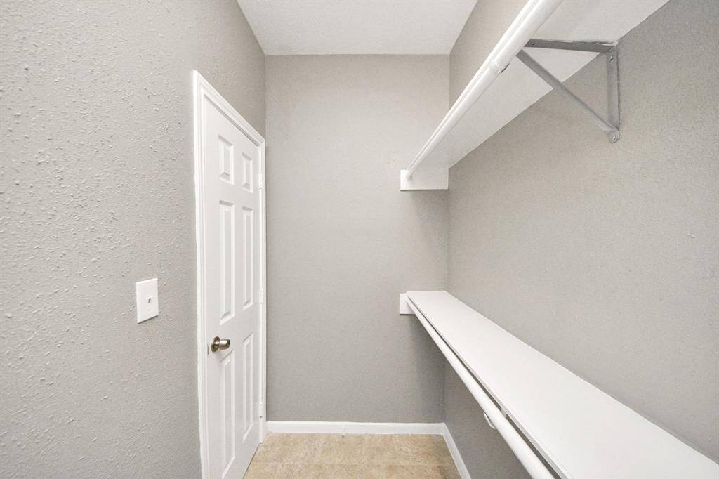 This photo shows a small walk-in closet with neutral-colored walls, a white door, and built-in shelves for storage.