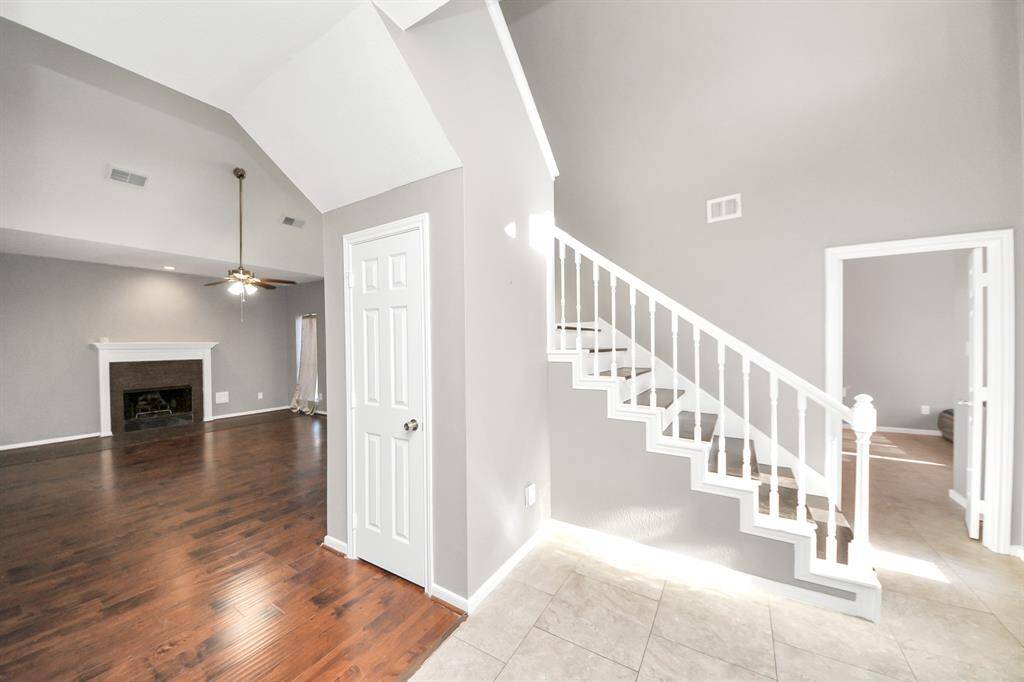 This home features an open living area with high ceilings, a cozy fireplace, and elegant wood flooring. The staircase leads to the second level, while neutral walls provide a bright and modern feel.