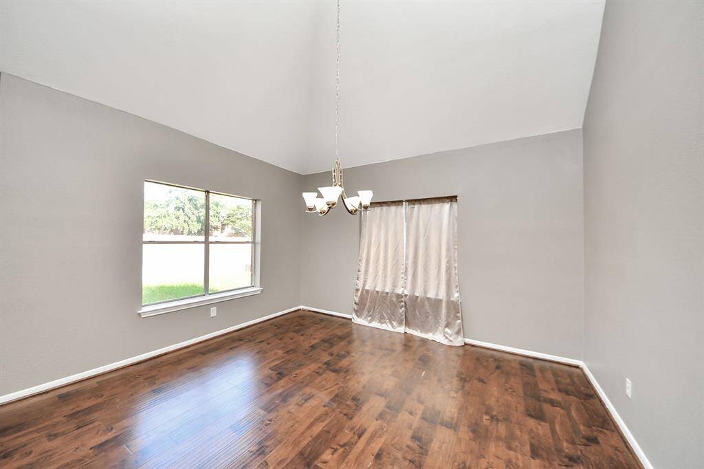Bright and spacious room with high ceilings, wood flooring, and large windows offering natural light. Features a modern chandelier and neutral wall colors, perfect for a dining or living area.