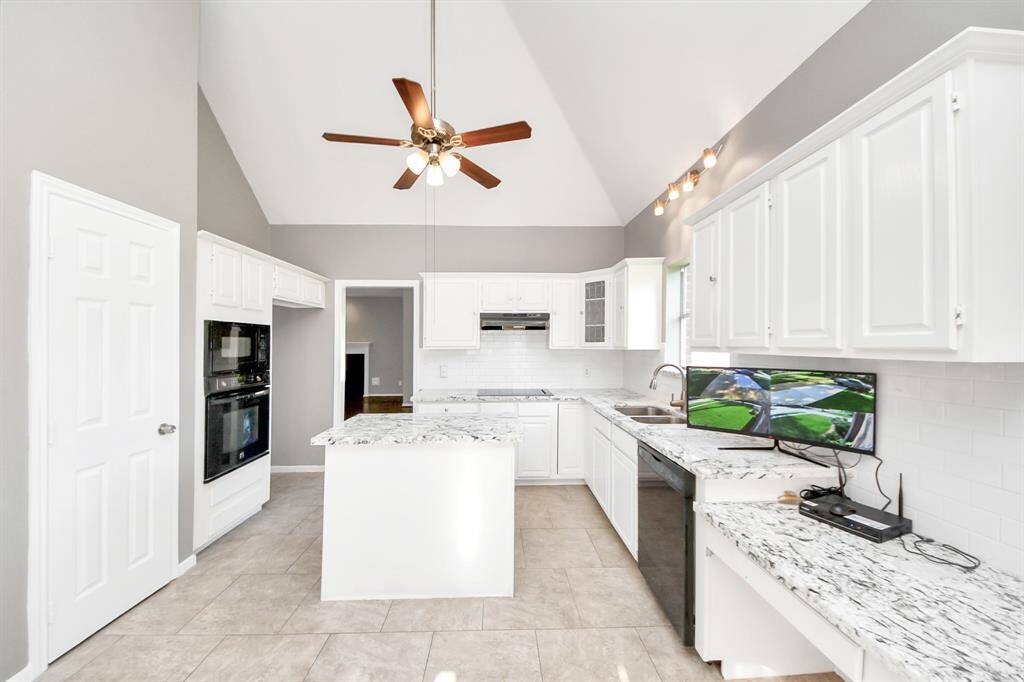 This bright kitchen features high vaulted ceilings, white cabinetry, and granite countertops. It includes a central island, double ovens, and modern appliances, with natural light streaming in to create an inviting space.