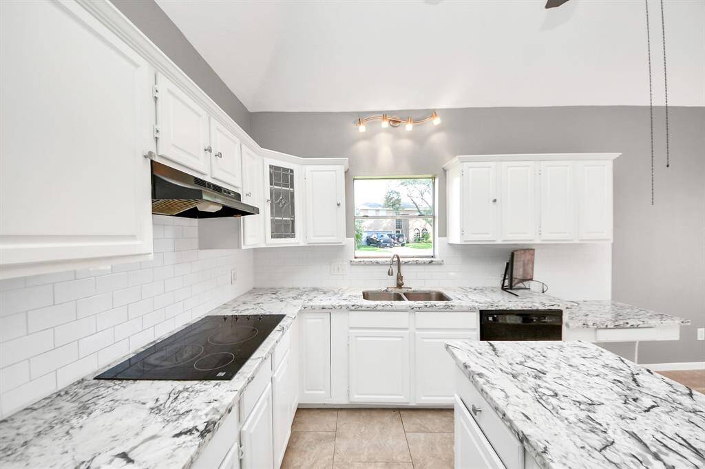 This kitchen features modern white cabinetry, marbled countertops, and a sleek electric cooktop. The backsplash is classic white subway tile, and there's ample natural light from the window above the sink.