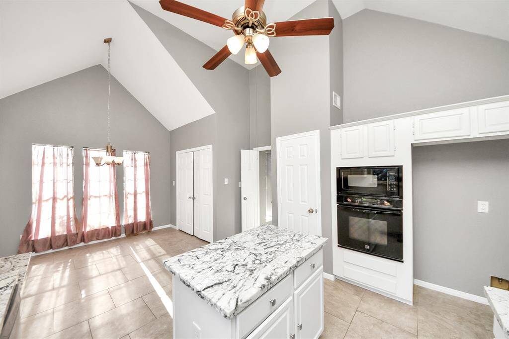 This bright kitchen features high vaulted ceilings, a central island with marble countertops, modern appliances, and ample natural light from large windows, creating an open and inviting space.