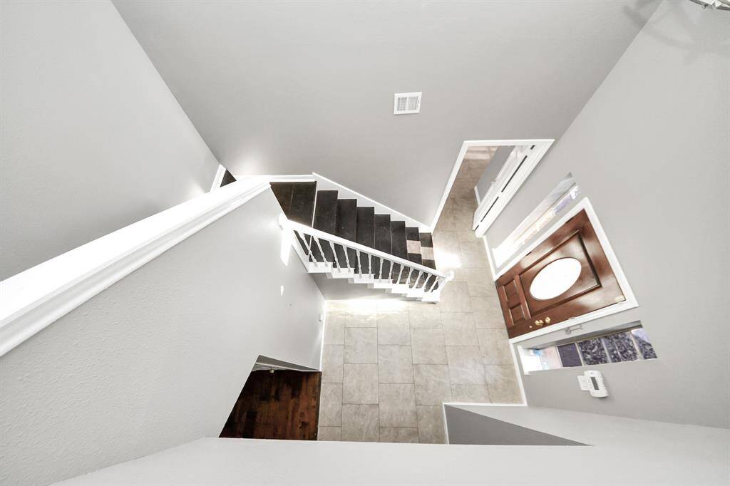 This photo showcases a bright, modern entryway with a wooden staircase and tiled floor. The open front door allows natural light to flood the space, highlighting the clean lines and neutral color palette.