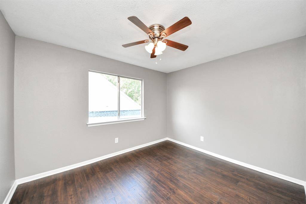 This room features a neutral gray color scheme, dark hardwood flooring, and a ceiling fan with lights. A window allows natural light, creating a bright and inviting space.