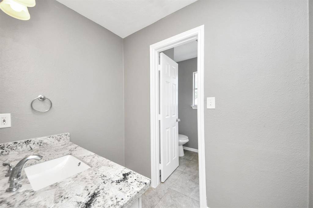 This bathroom features a modern design with gray walls, a granite countertop, and a sleek faucet. It includes a toilet in a separate alcove, adding privacy.