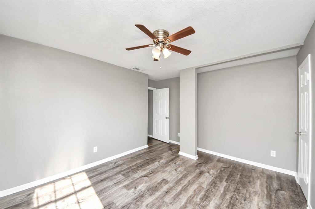 This room features fresh gray walls, wood-look flooring, and a ceiling fan. Natural light streams in, creating a bright, welcoming space. Ideal for a bedroom or office.