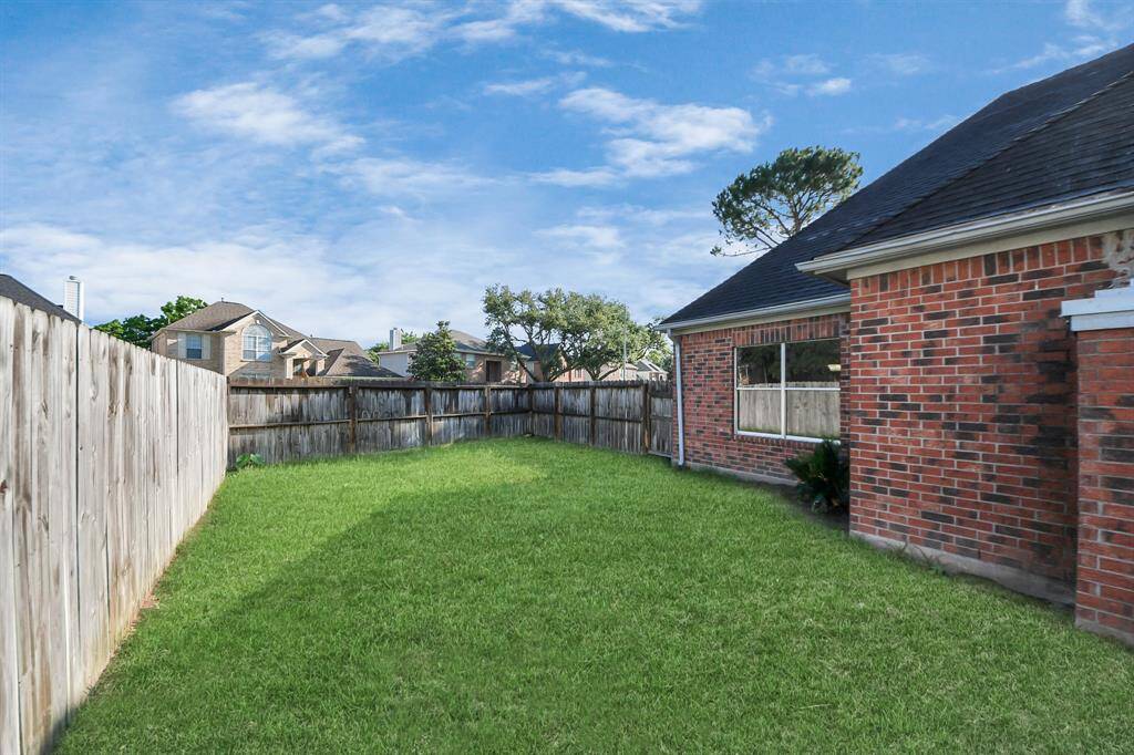 This photo shows a spacious backyard with well-maintained grass, surrounded by a wooden fence. The side of a brick house is visible, offering a private and open outdoor area.