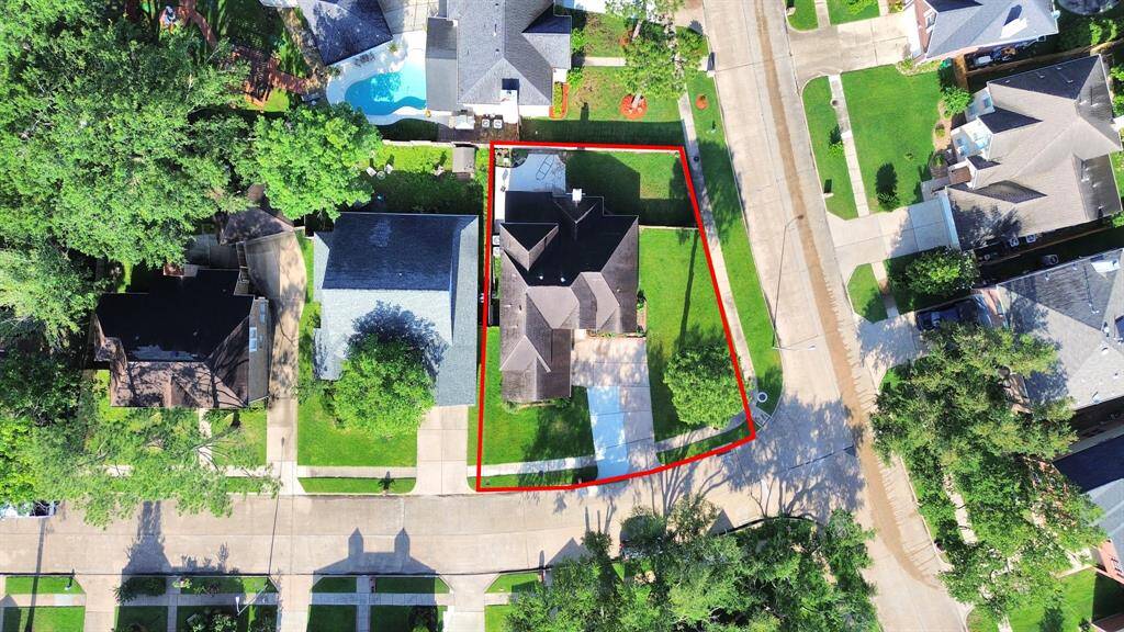 This aerial photo showcases a well-maintained home with a spacious yard, highlighted by a red boundary. It's situated in a suburban neighborhood with tree-lined streets and nearby houses, offering a welcoming and family-friendly environment.
