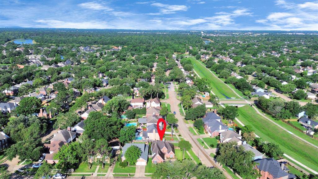This aerial photo showcases a suburban neighborhood with tree-lined streets and well-maintained homes. A red marker highlights a specific property. The area appears to be green and spacious, with proximity to a waterway or canal, offering a serene and picturesque setting.