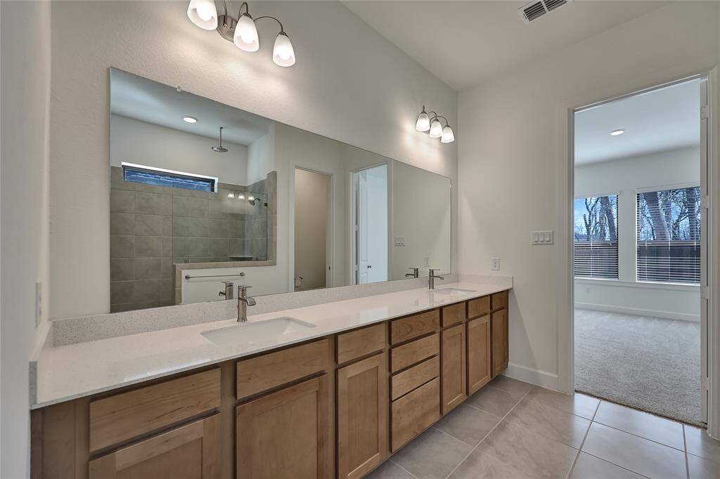 The primary bathroom has a huge frameless mirror, tile floors, and plenty of cabinet space.