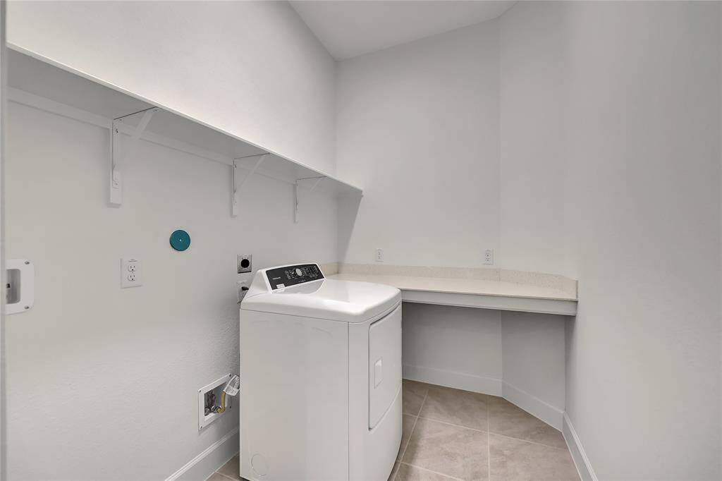 The laundry room features tile floors, washer and dryer connections, and shelving with plenty of storage space.