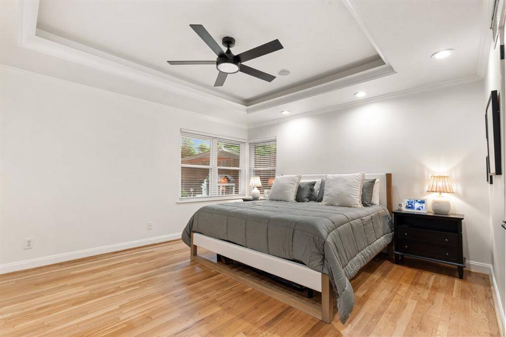 Oversized primary suite showcases coffered ceiling, modern ceiling fan, window view of backyard, gleaming hardwood floors and two large closets.